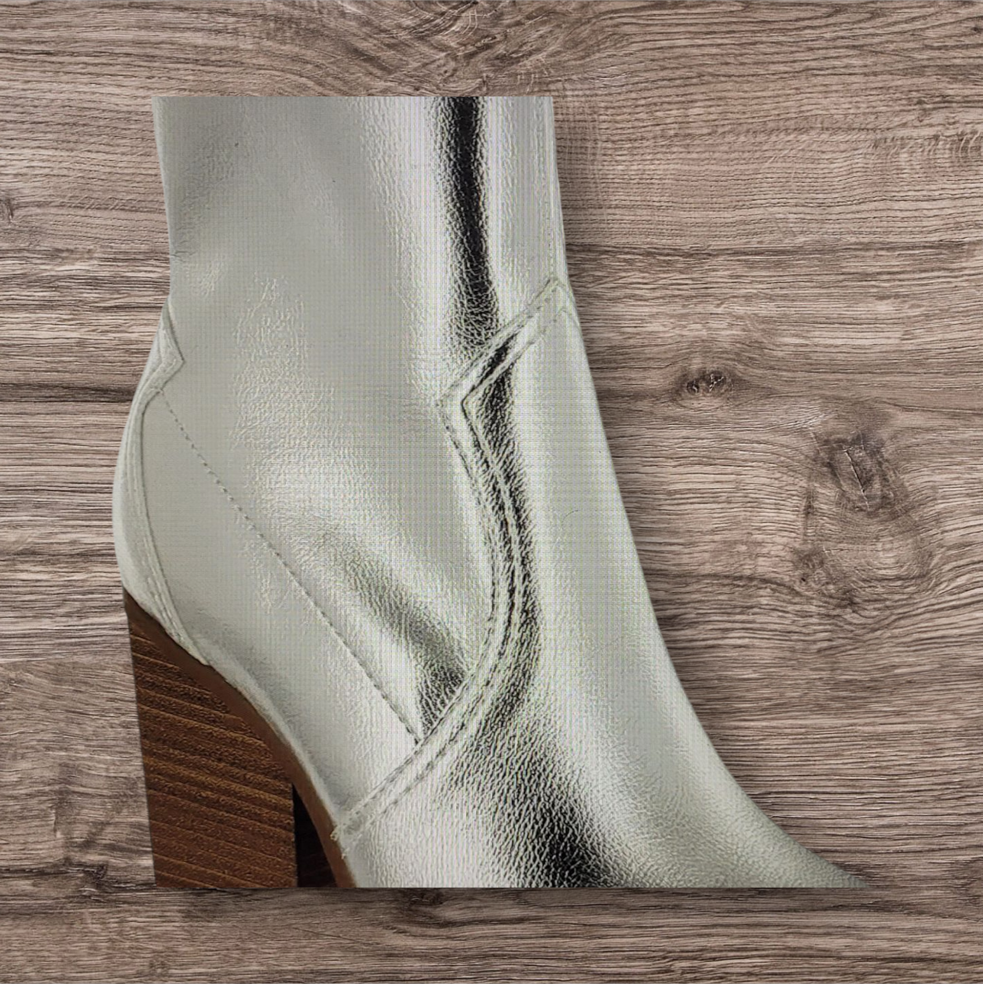Silver metallic ankle boot with a brown block heel on a wooden surface